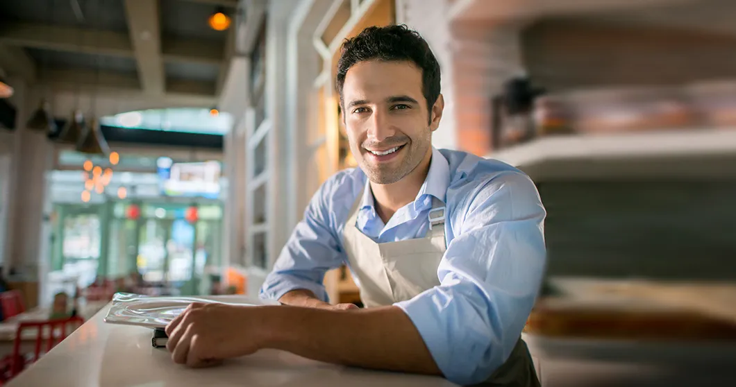 Hombre joven que está de pie junto a una barra de café y mira hacia la cámara..