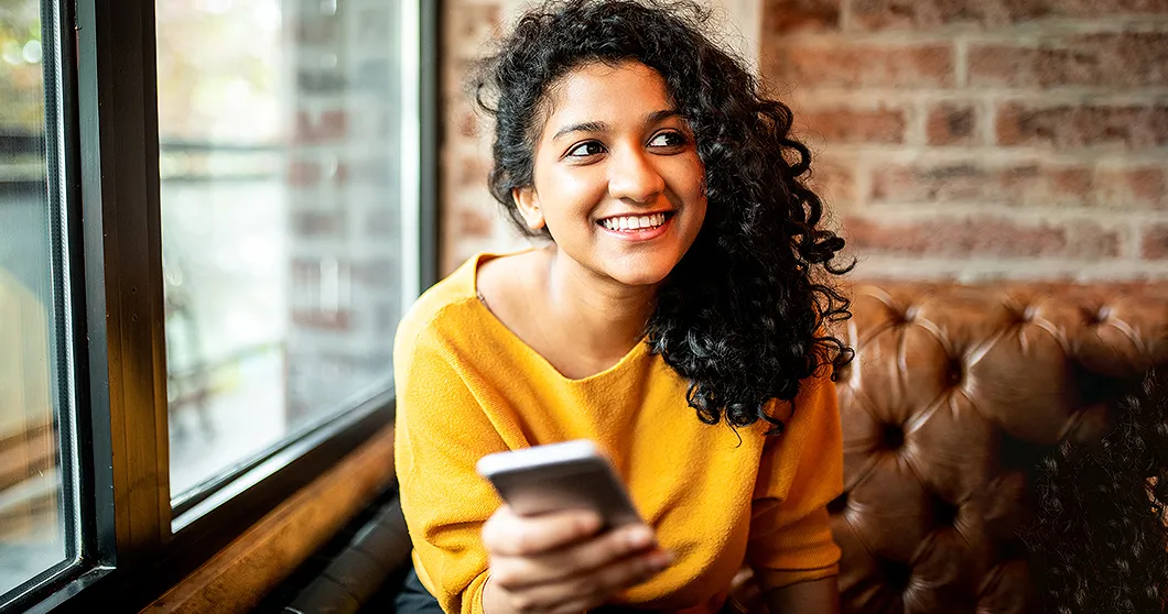 Lachende jonge vrouw zit op een bank en houdt een smartphone vast
